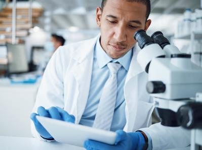 Microscope, science and man with tablet in laboratory for research, medical analysis and biotechnology. Scientist, microbiology and investigation with digital technology, dna testing and development.